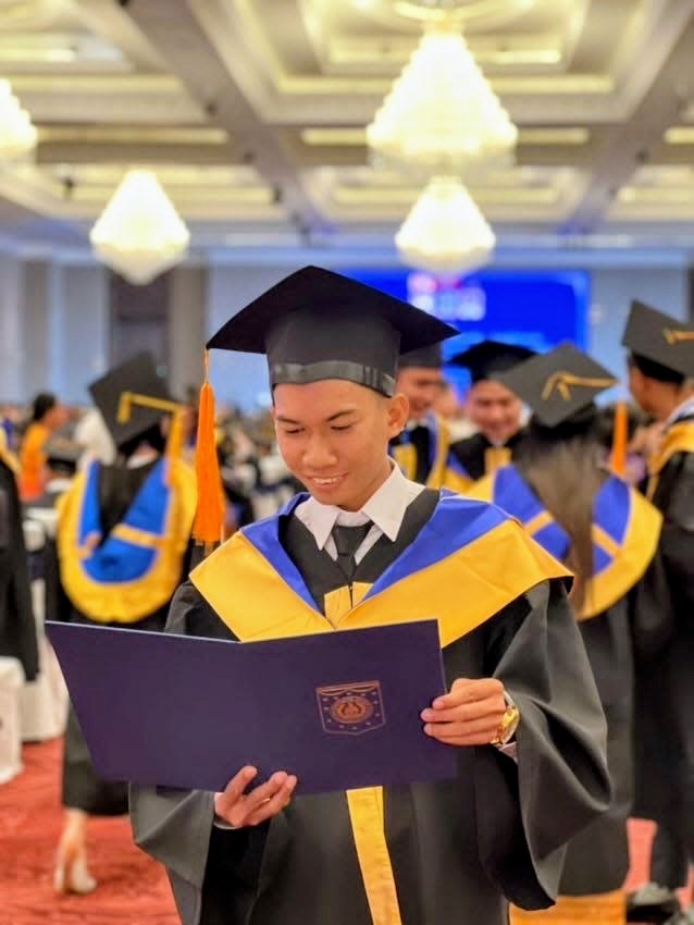 A graduate in cap and gown reading his diploma