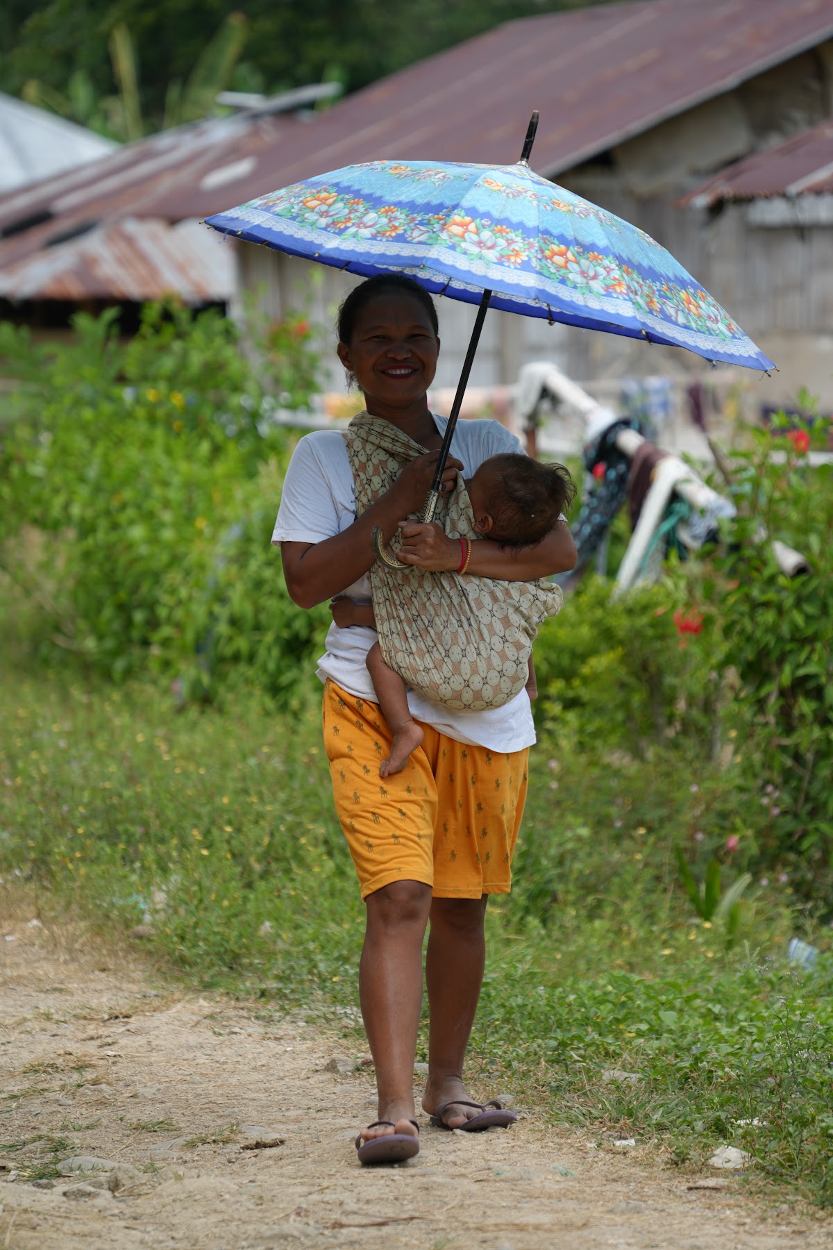 A mother carrying her baby under a blue umbrella
